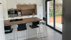 Eine moderne Küche mit weißen Schränken, einer Holz Arbeitsplatte, Edelstahlgeräten und einer großen Schiebeglastür zum Außenbereich.