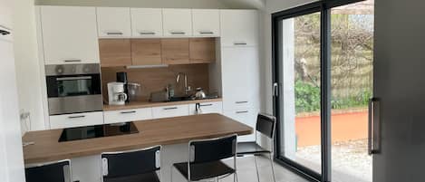Una cocina moderna con armarios blancos, encimera de madera, electrodomésticos de acero inoxidable y un amplio ventanal corredero al exterior.