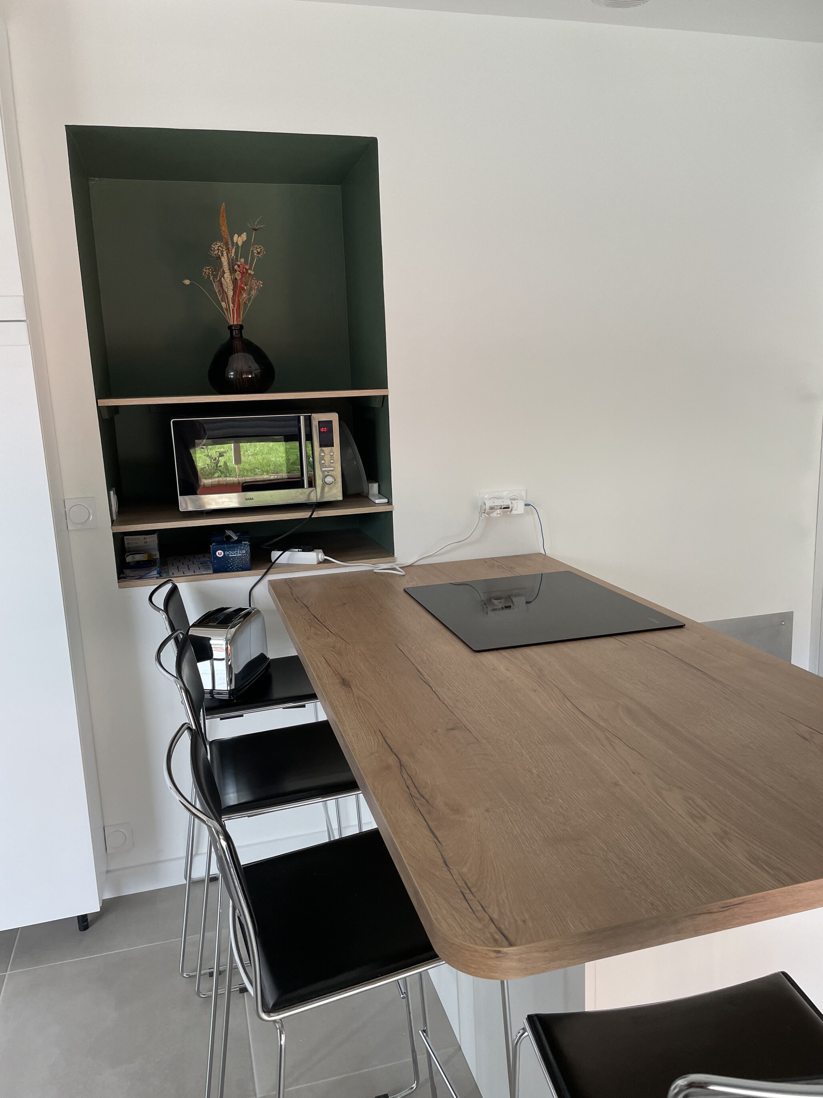 Eine moderne Küche mit einem Holztisch, schwarzen Stühlen, einer Mikrowelle und einer Vase mit getrockneten Blumen.
