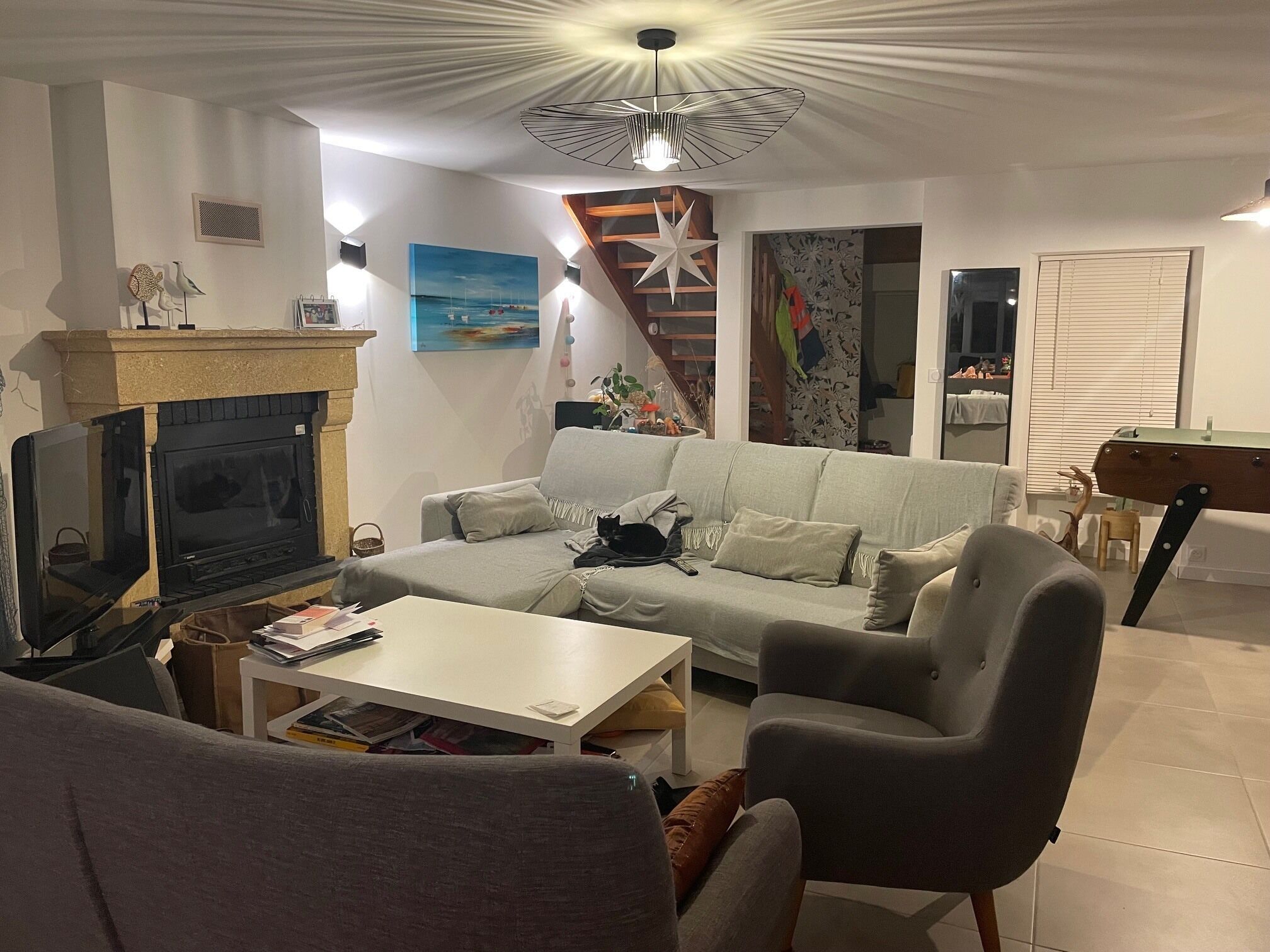 Un salón con chimenea, sofá, mesa de centro, televisor y una lámpara de techo en forma de estrella.