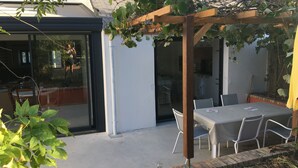 Ein Patio mit Pergola, die mit Weinreben bewachsen ist, einem Tisch mit Stühlen und einer Glastür, die zu einem Innenraum führt.