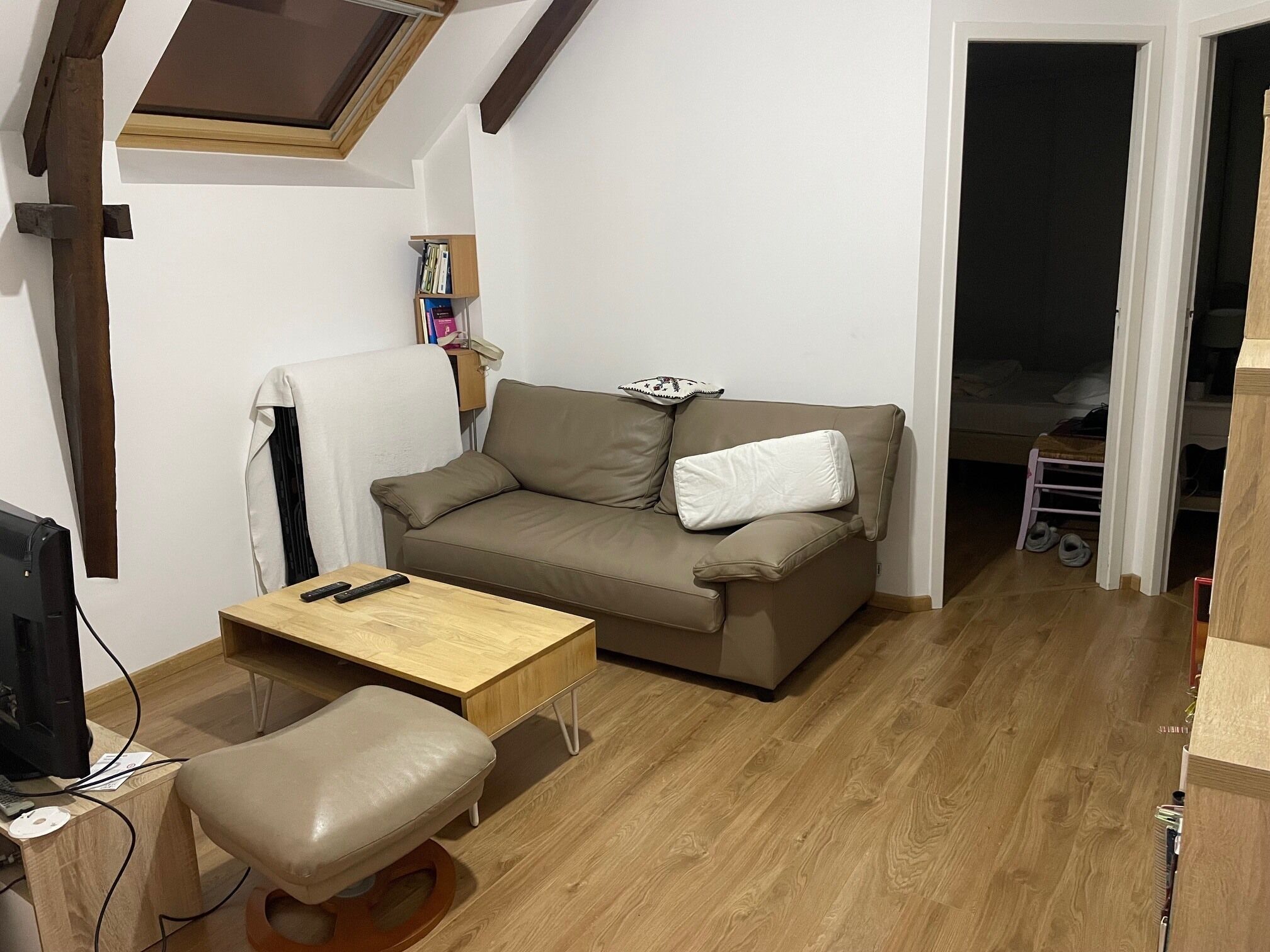 Et værelse med sofa, lille bord, stol, fjernsyn og bogreol.