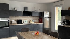 A modern kitchen with dark cabinetry, a wooden dining table, and a fruit bowl.