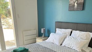 A bedroom with a bed, pillows, a nightstand, a lamp, and a painting on the wall.