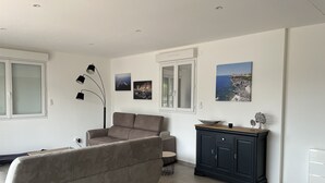 A modern living room with a grey sofa, a dark wooden cabinet, and a floor lamp. There are three framed pictures on the wall.