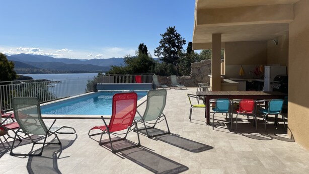 A poolside area with lounge chairs, a barbecue grill, and a view of the mountains.