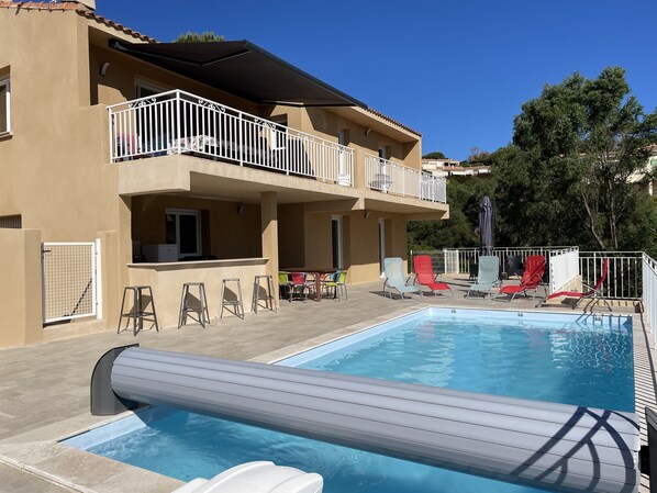 A two-story building with a swimming pool, outdoor seating, and a covered patio area.