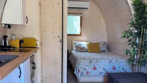 Um quarto compacto com arco, cozinha compacta, cama com roupa de cama florida e um vaso de planta.