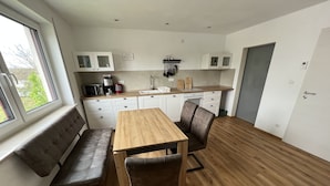 A modern kitchen with white cabinets, a wooden dining table, and a bench. - Vacation apartment "Saumpfad" 25 minutes to Legoland (Horgau)