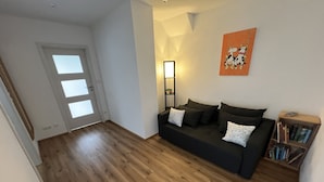 A living room with a dark sofa, wooden flooring, a door with frosted glass panels, a wall-mounted mirror, and a bookshelf. - Vacation apartment "Saumpfad" 25 minutes to Legoland (Horgau)