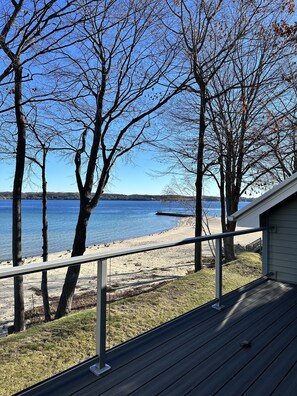 A deck with a view of a lake and beach, surrounded by trees. - Condo in world class Leelanau Peninsula, Suttons Bay Beach Condo (Suttons Bay)