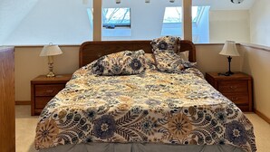 A bedroom with a large bed, two nightstands, a ceiling fan, and a window with a view. - Condo in world class Leelanau Peninsula, Suttons Bay Beach Condo (Suttons Bay)