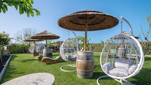 Espaces de détente en plein air avec des fauteuils suspendus et des parasols en chaume, le tout entouré de verdure.