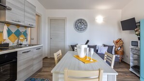 Une cuisine moderne avec des meubles gris, un four encastré et un coin repas comprenant une table blanche et un set de table jaune.