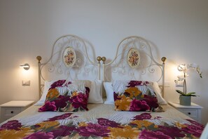 Un lit double avec une literie à motifs floraux, une tête de lit décorative, des lampes de chevet et une petite plante en pot.
