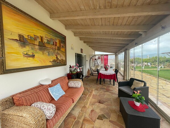 Une pièce chaleureuse avec un sol en pierre, un plafond en bois, un grand tableau, un canapé, une table à manger avec des chaises et une vue sur l’extérieur.