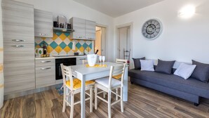 Une cuisine moderne avec des meubles blancs, une table à manger avec des chaises, un canapé gris et une horloge murale.