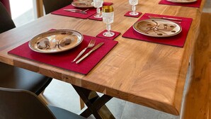 Ein Esstisch ist gedeckt mit Tellern, Besteck und Gläsern, mit roten Platzsets und einer Holztischplatte.