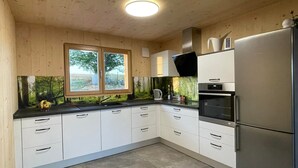 Eine moderne Küche mit weißen Schränken, einem Edelstahlkühlschrank und einem Fenster mit Blick auf Bäume.