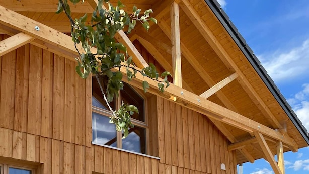 Ein Holzgebäude mit großen Fenstern und einer überdachten Veranda mit Holzliegen.
