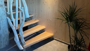 Eine Holztreppe mit einer modernen Leuchte darüber und einer Topfpflanze daneben.