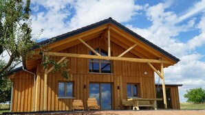 Eine Holzhütte mit Satteldach, großen Fenstern und einer überdachten Sitzterrasse.