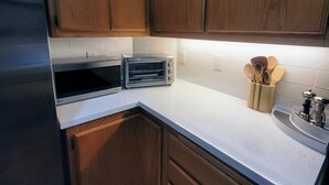 Een keuken met houten kasten, een roestvrijstalen koelkast, een toasteroven en een spoelbak met een houten houder voor keukengerei.