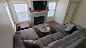 Een woonkamer met een grote grijze modulaire bank, een open haard, een flatscreen televisie en een salontafel.