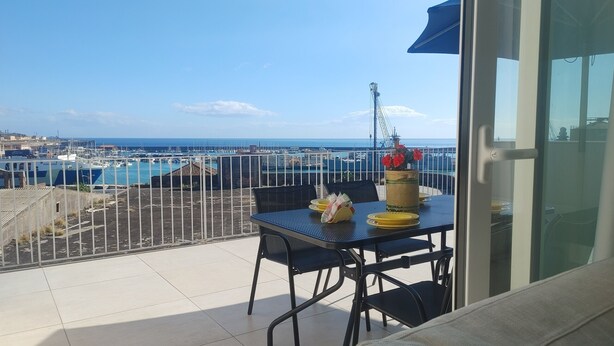 A balcony with a table set for dining, overlooking a marina with boats and a clear sky. - PENTHOUSE ON CATANIA HARBOR AND VOLCANO VIEW A FEW STEPS FROM CATHEDRAL (Catania)