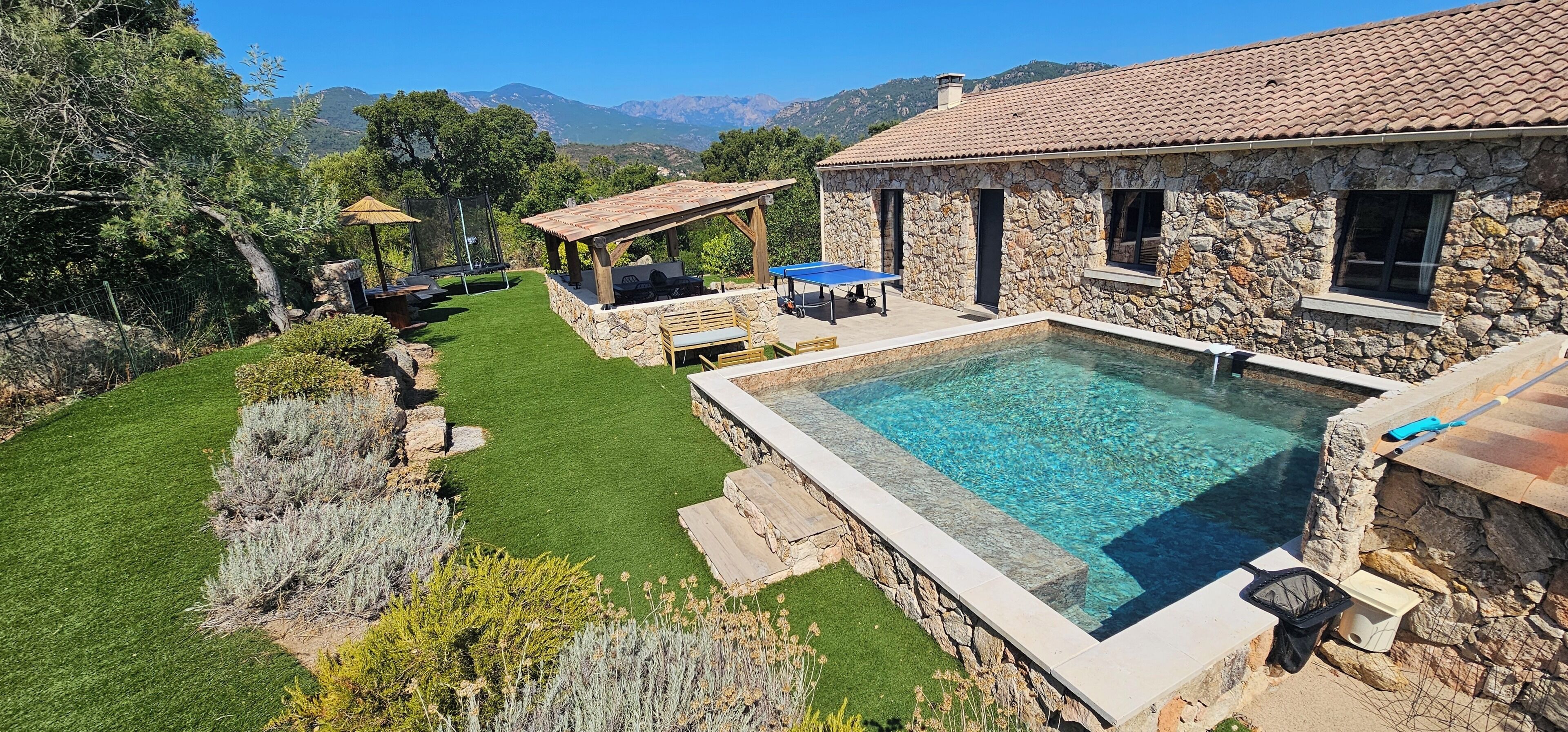 A stone building with a swimming pool, outdoor seating, and a view of mountains.