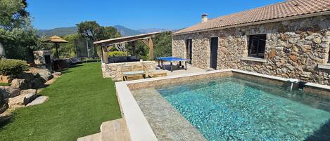 Un espace piscine agrémenté d’une maison en pierre, d’une terrasse en bois et d’une pelouse verdoyante.
