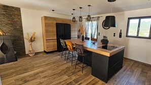 Een moderne keuken met een houten kookeiland, barstoelen, hanglampen en een groot raam met uitzicht.