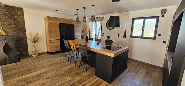 A modern kitchen with a wooden island, bar stools, pendant lighting, and a large window with a view.
