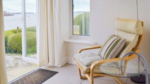 Une pièce avec vue sur un plan d’eau, un fauteuil avec des coussins, une table et une lampe.