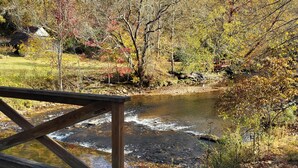 Un pont en bois enjambant un ruisseau, avec des feuilles d’automne en arrière-plan.