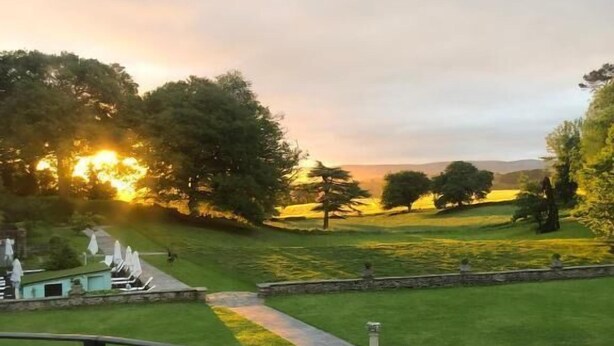 Un patio con mobiliario exterior y vistas a un paisaje cubierto de césped al atardecer.