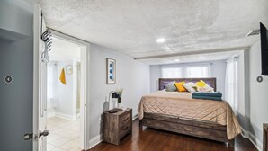 A bedroom with a wooden bed, a nightstand, and a door leading to another room. - Charming Seminole Heights Stay with Free Parking (Tampa)