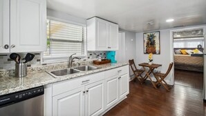 A modern kitchen with white cabinets, granite countertops, and a dishwasher. There is a dining area with a wooden table and chairs. - Charming Seminole Heights Stay with Free Parking (Tampa)