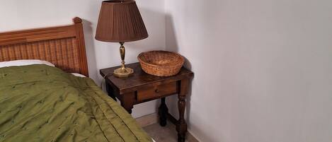 Un dormitorio con una colcha verde, una mesita de noche de madera con una lámpara y una cesta de mimbre.