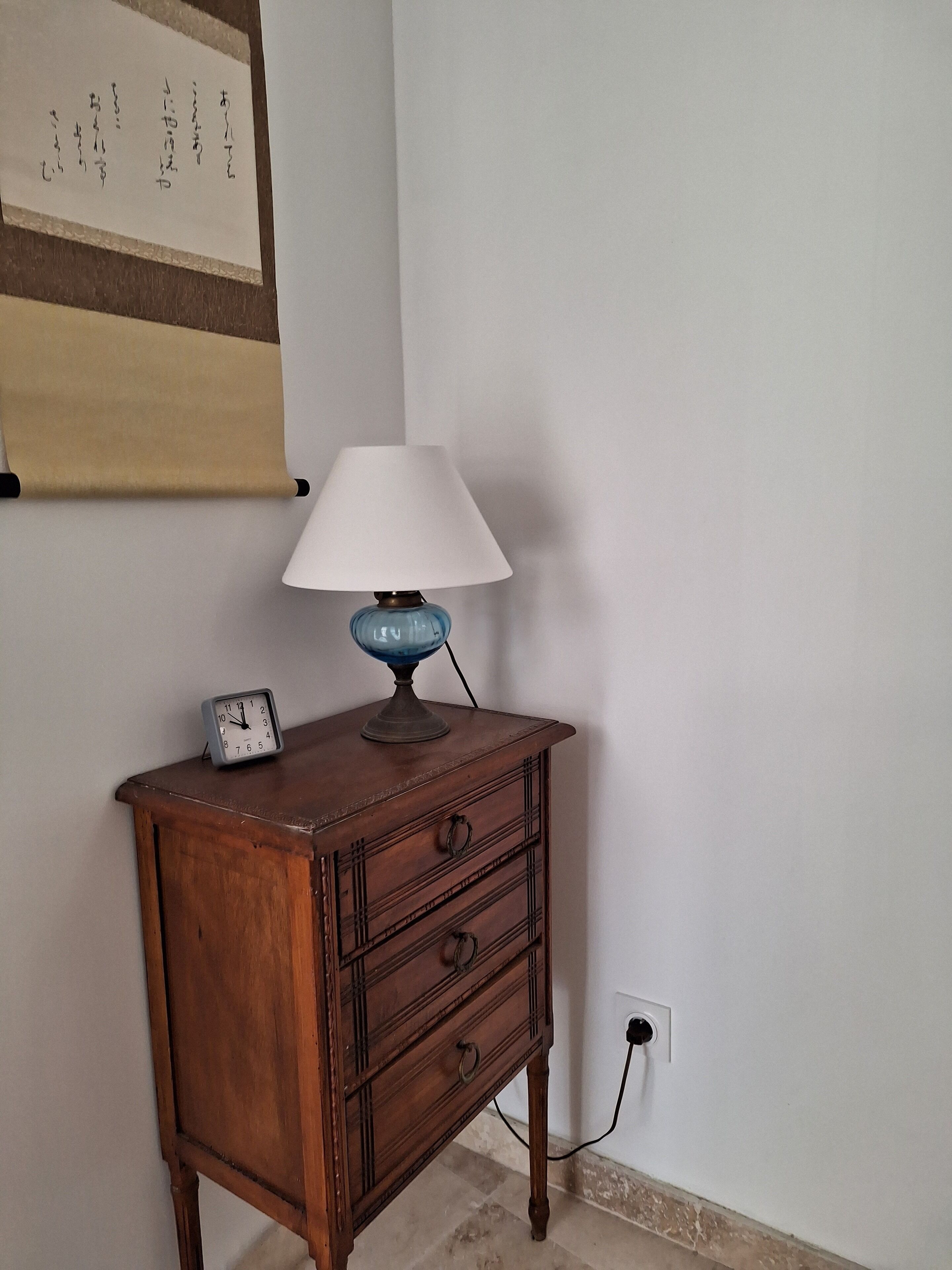 Une table de chevet en bois, avec une lampe bleue et une horloge.