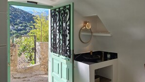 Habitació amb vista a un paisatge de muntanyes a través d'una porta oberta, un lavabo blanc amb taulell negre i una làmpada decorativa al sostre.