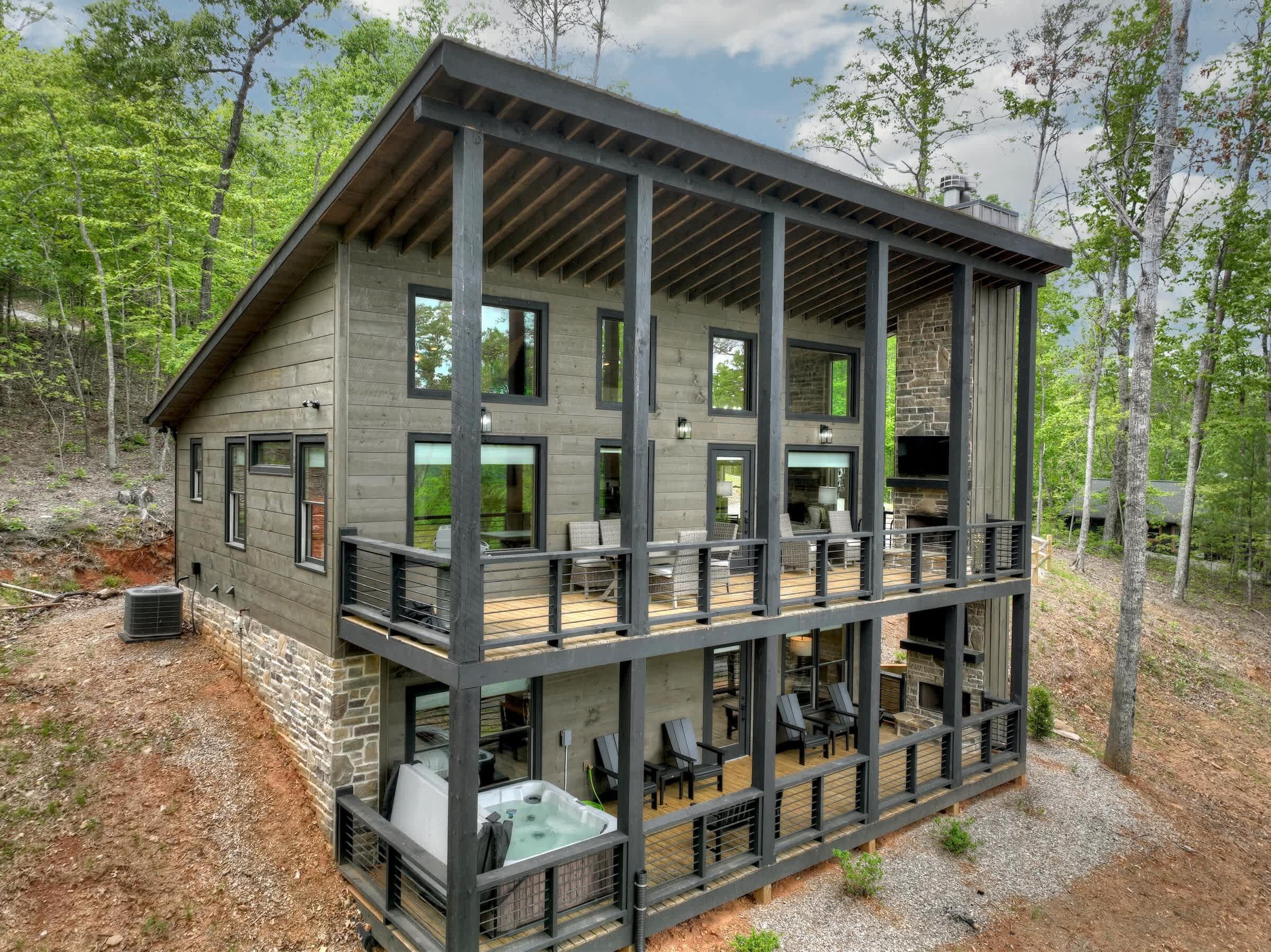 A multi-story cabin with a balcony, outdoor seating, and a hot tub.