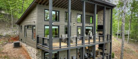 A multi-story cabin with a balcony, outdoor seating, and a hot tub.