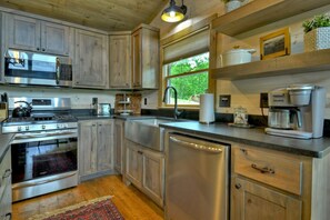 A modern kitchen with stainless steel appliances, wooden cabinets, and a large window offering a view of greenery.