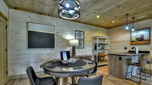 Een houten interieur met een ronde eettafel, stoelen, een kroonluchter en een keukenbar met barstoelen.