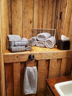 A wooden bathroom with a towel rack, a basket of folded towels, and a tissue box. - Hooked On A Feeling — Fishing Cabin (Rising Fawn)