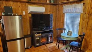 Una cocina compacta con un refrigerador de acero inoxidable, un horno empotrado, un televisor y una zona de comedor con una mesa y sillas.