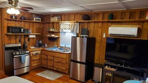Una cocina compacta con armarios de madera, refrigerador, microondas, estufa, lavamanos y un pequeño comedor con mesa y sillas.