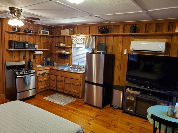A compact kitchen with wooden cabinets, a refrigerator, microwave, stove, sink, and a small dining area with a table and chairs. - Hooked On A Feeling — Fishing Cabin (Rising Fawn)