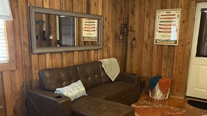 Una sala de estar acogedora con un sofá seccional de cuero marrón, un tapete estampado y paredes de madera.